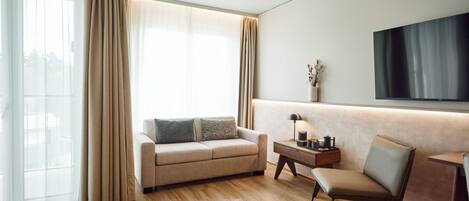 A modern living room with a sofa, a chair, a side table, and a flat-screen TV mounted on the wall.