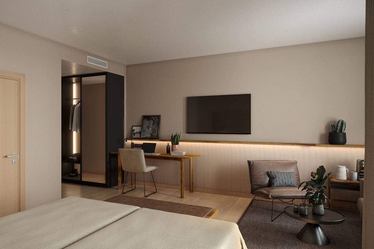 A hotel room with a bed, a desk with a chair, a TV mounted on the wall, and a small table with a plant.