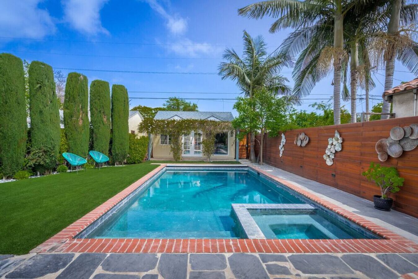 Une piscine rectangulaire bordée de briques, entourée d’une pelouse bien entretenue et de grands arbres.