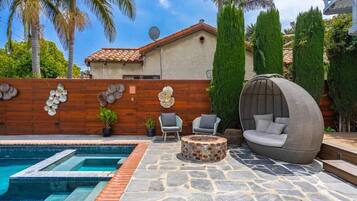 A swimming pool with stone tiles, a wooden wall with decorative shells, and a round seating area with cushions.