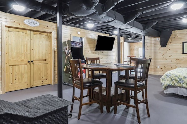 A room with a wooden door labeled 'laundry,' a table with chairs, a bed with a floral bedspread, and a mounted television.