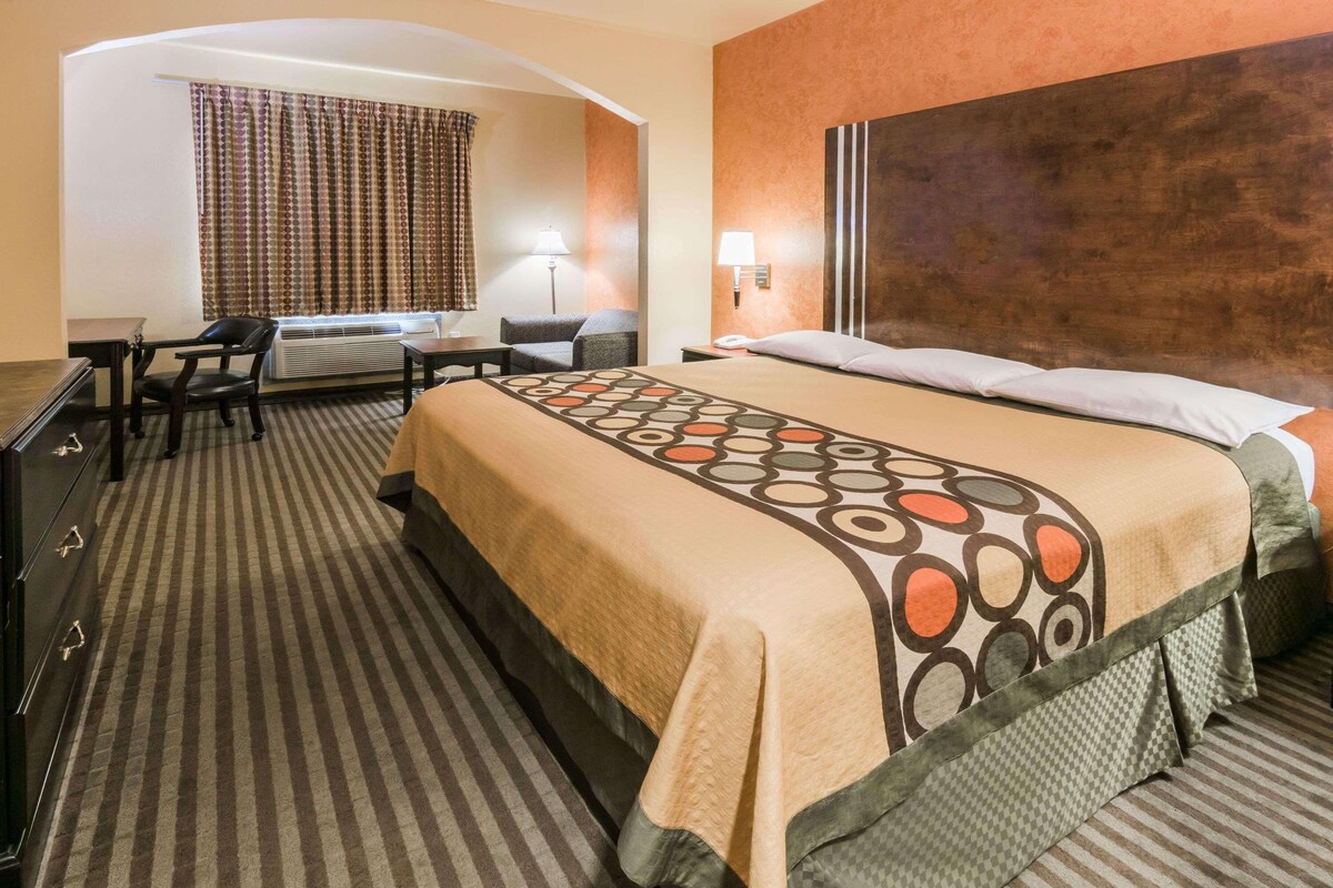 A hotel room with a large bed, a desk, a chair, a lamp, and a window with curtains.