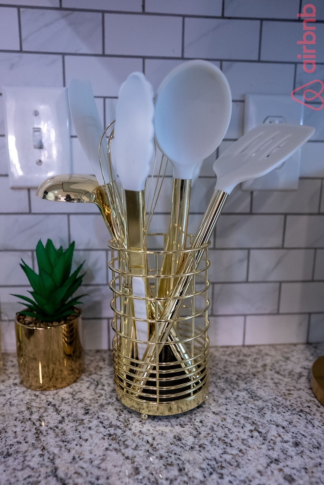 A kitchen counter with a gold wire basket holding white kitchen utensils.