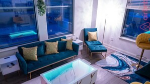 A modern living room with a teal sofa, a glass coffee table, and a yellow chair. - Luxurious Downtown Indy City View Apartment!  (Indianapolis)
