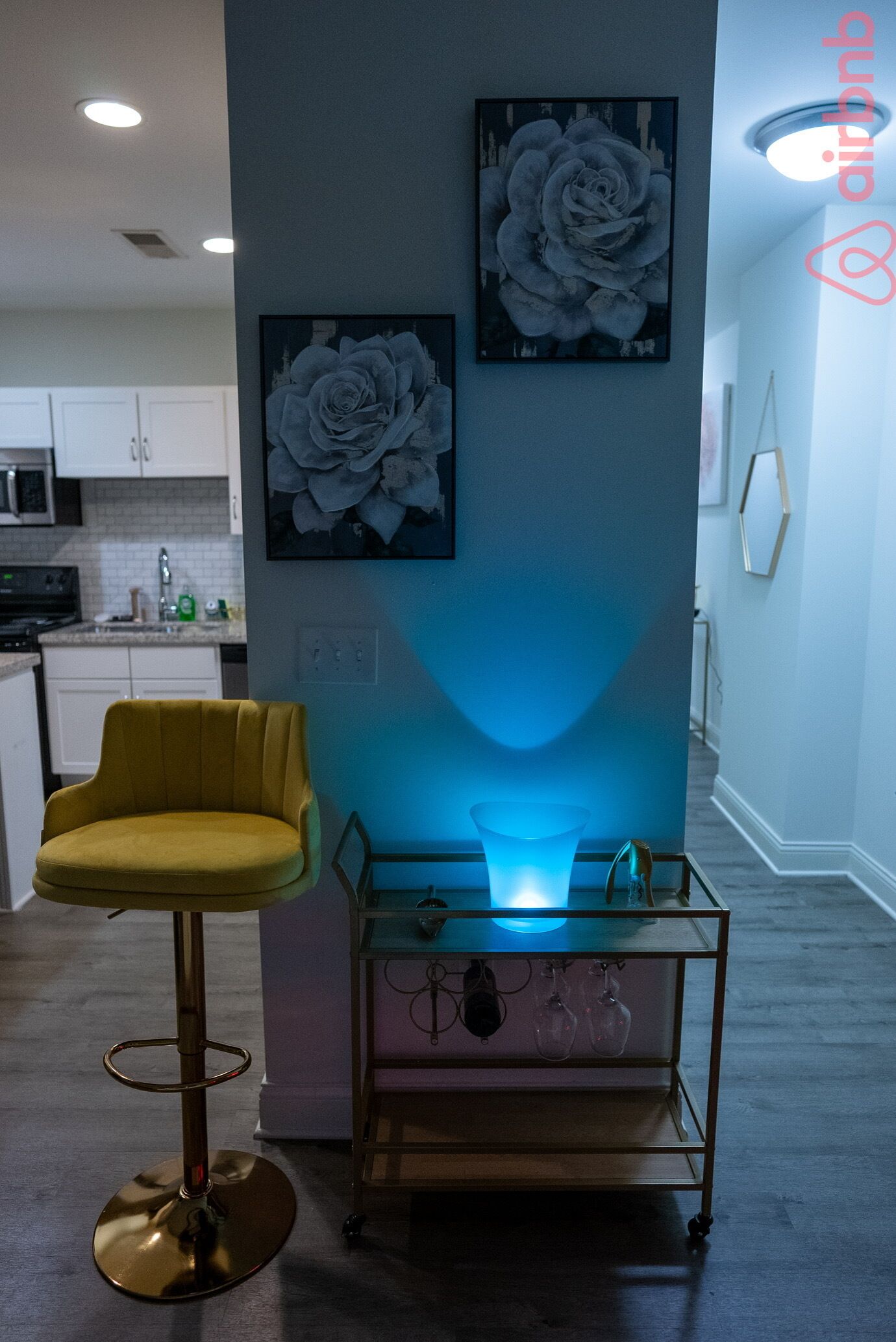 A modern kitchen with white cabinets, a yellow chair, and a glass table with wine glasses.