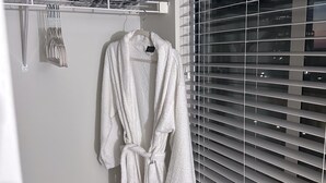 A bathroom with a white bathrobe hanging on a hook, a towel rack with folded towels, and a window with blinds. - Luxurious Downtown Indy City View Apartment!  (Indianapolis)