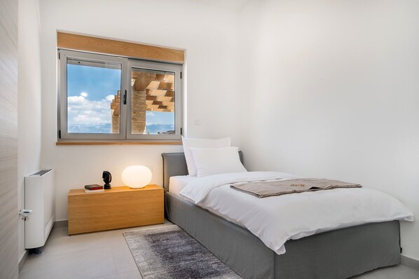 A bedroom with a bed, bedside table, lamp, and a window with a view of mountains.
