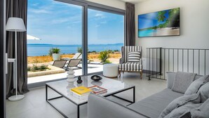 A modern living room with a large sliding glass door leading to a balcony with a view of the sea. There is a sofa, a chair, and a coffee table with books and decorative items. - Villa La Isla with Pool II (Novalja)