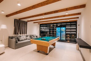 Uma sala de estar moderna com mesa de bilhar, um sofá e um espaço de bar com prateleiras cheias de garrafas.