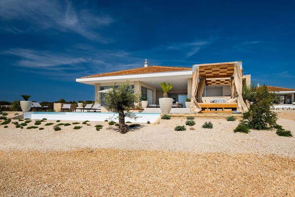 A modern villa with a swimming pool, outdoor seating, and a view of the sea.