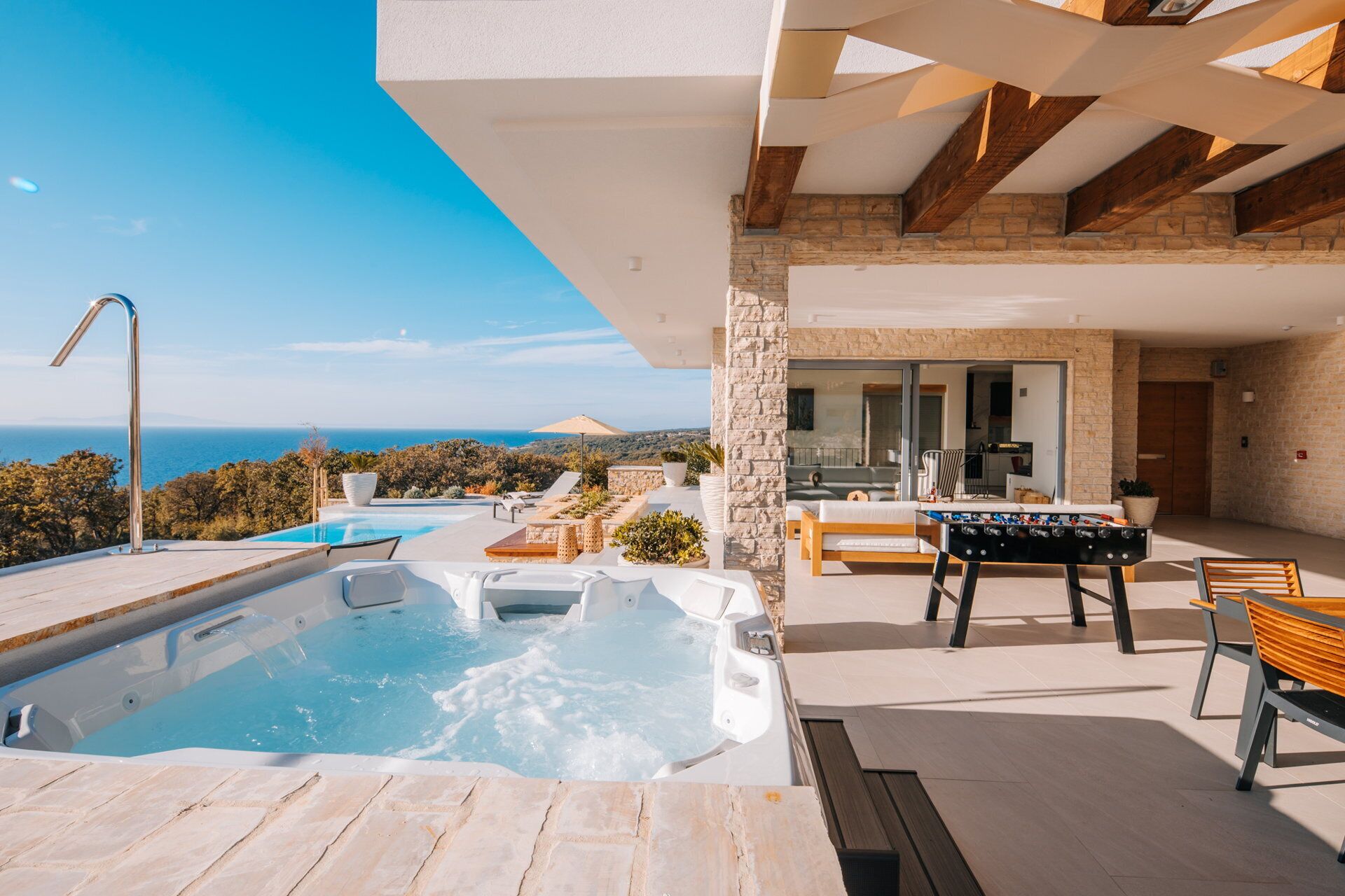 A modern outdoor pool area with a hot tub, lounge chairs, and a foosball table.
