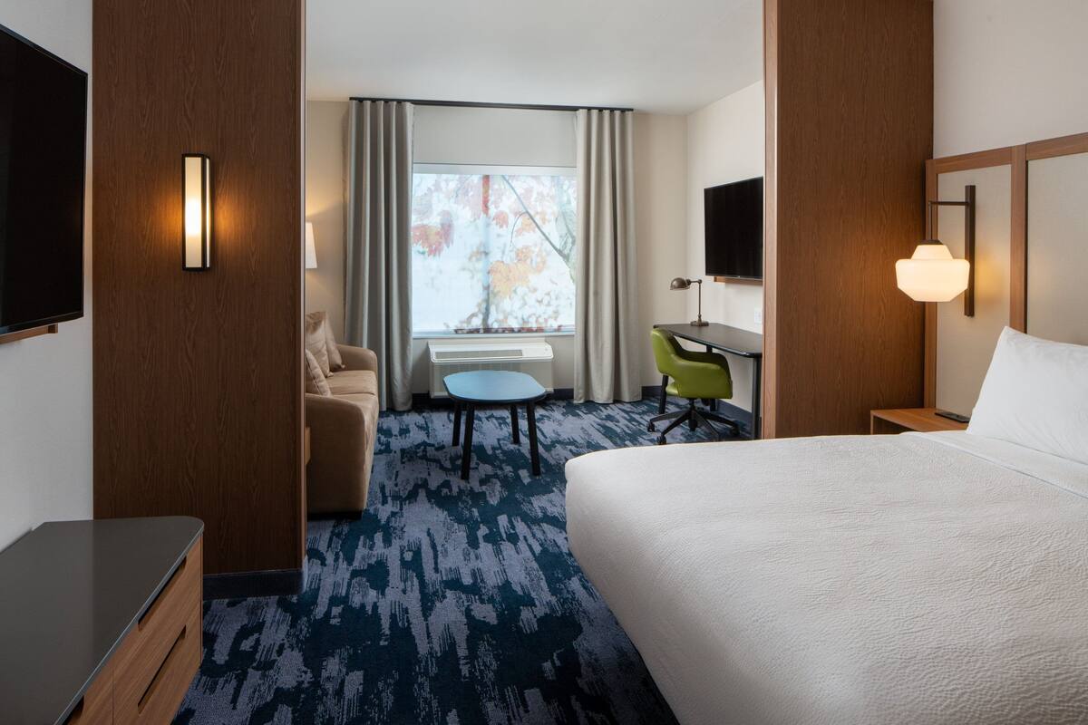 Une chambre d’hôtel avec un grand lit, un bureau, une chaise, une télévision et une fenêtre avec des rideaux.