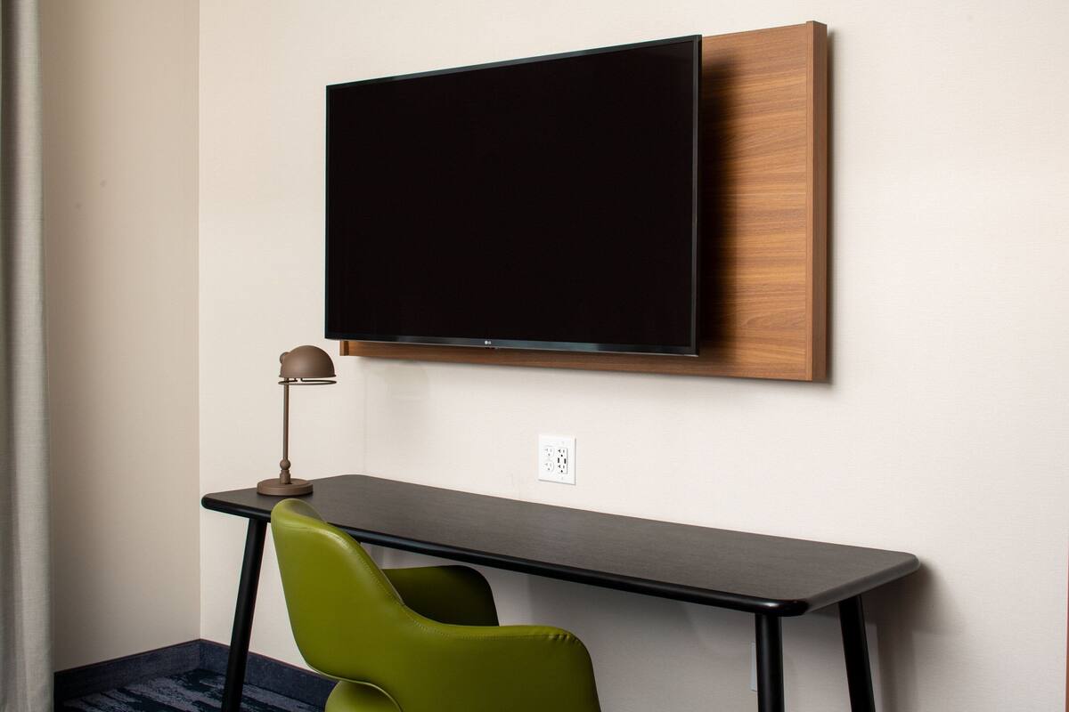 Une chambre d’hôtel moderne équipée d’un téléviseur à écran plat fixé au mur, d’un petit bureau avec une chaise et d’une lampe.