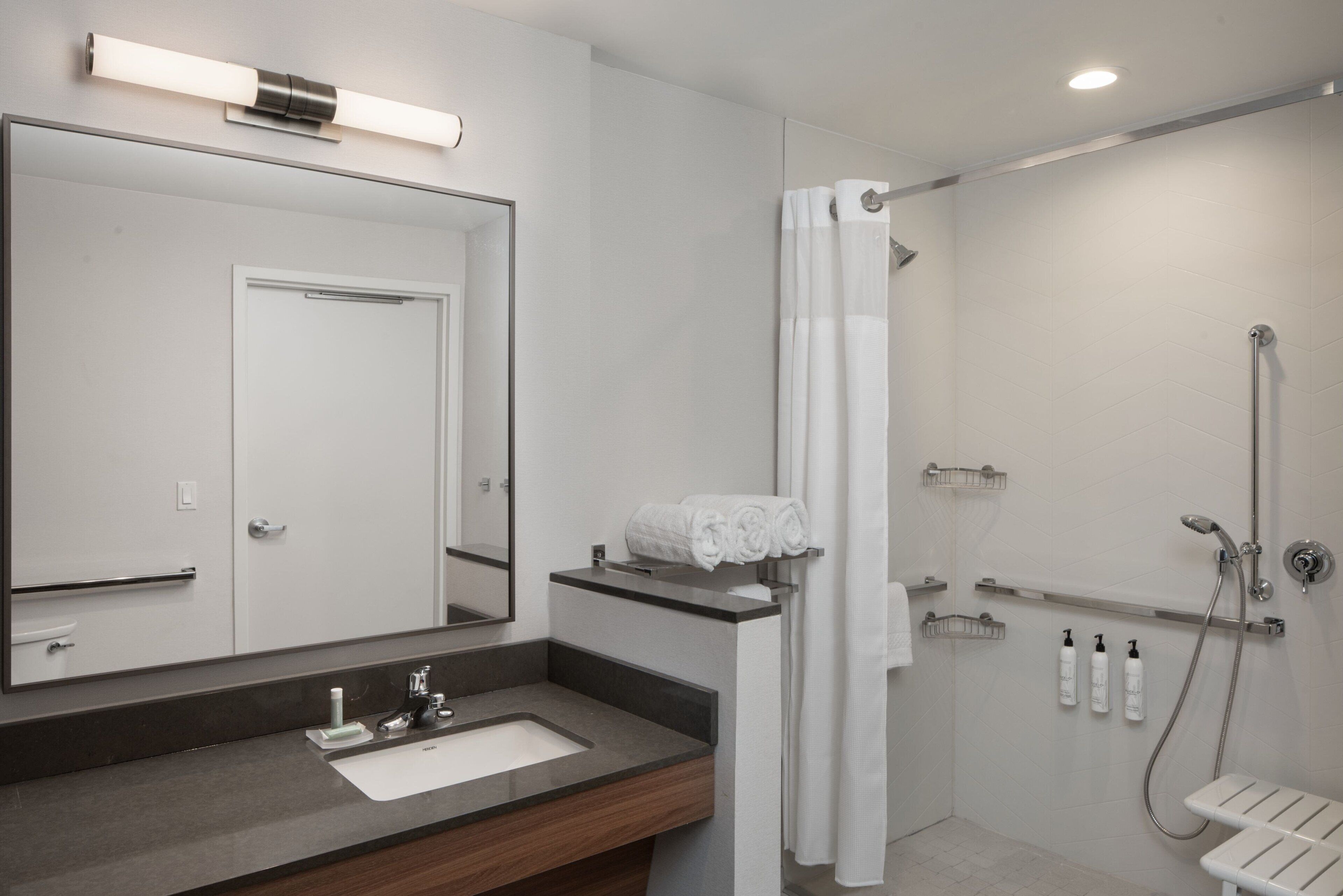 A modern bathroom with a large mirror, a sink, a shower with a handheld showerhead, and a towel rack.