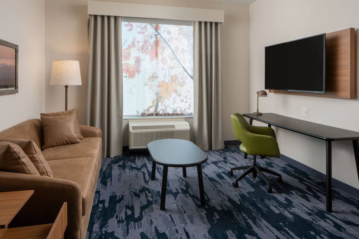 Une chambre d’hôtel équipée d’un canapé, d’une petite table, d’un bureau avec une chaise, d’un téléviseur fixé au mur et d’une fenêtre avec des rideaux.