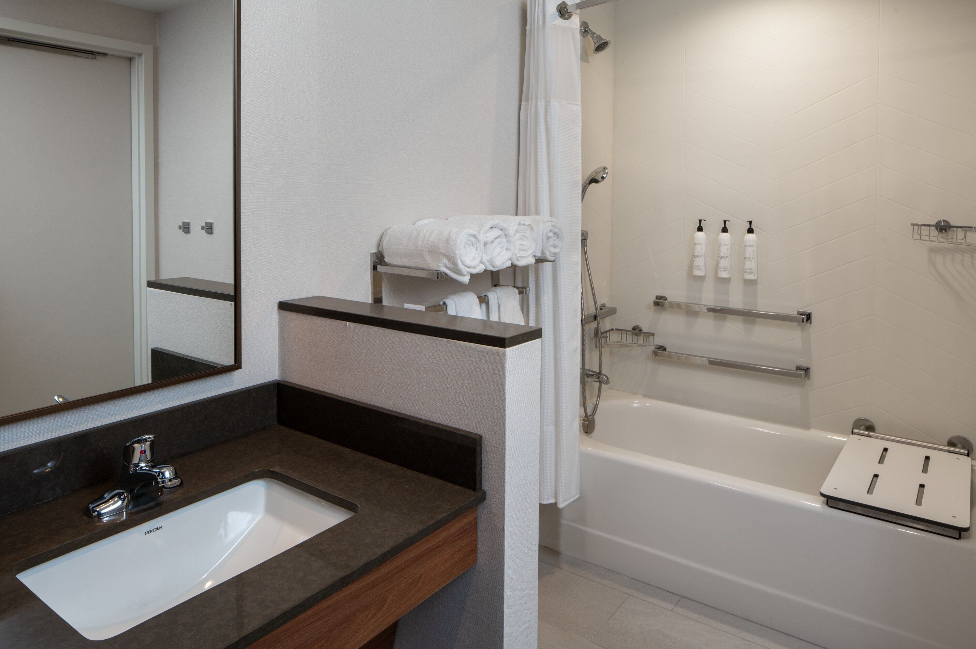 Une salle de bain moderne équipée d’un lavabo, d’un miroir, d’une douche et d’un porte-serviettes.