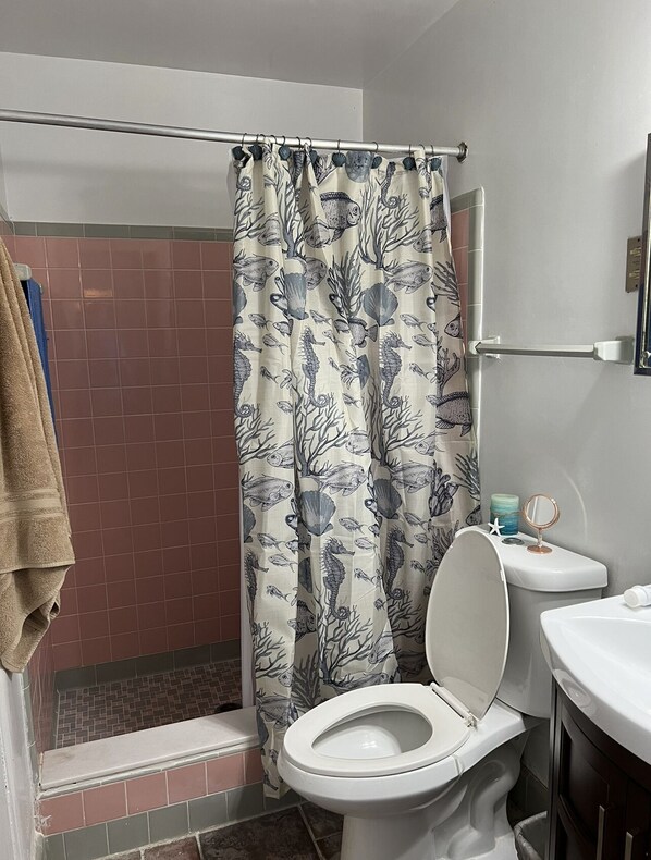 Une salle de bain avec un rideau de douche orné d’un motif représentant la vie marine, des toilettes, un petit lavabo avec un miroir et une serviette accrochée au mur.