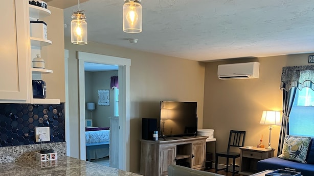 A modern kitchen with granite countertops, a dining area with a white table and chairs, a living room with a sofa and TV, and a hallway leading to another room. - 2 Bed/1 Bath Saunders Bay Gilford with boat slip. Walk to Meadowbrook for a show (Gilford)