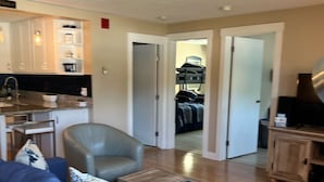 A living room with a blue sofa, a wooden coffee table, and a kitchen area with cabinets and a sink. - 2 Bed/1 Bath Saunders Bay Gilford with boat slip. Walk to Meadowbrook for a show (Gilford)