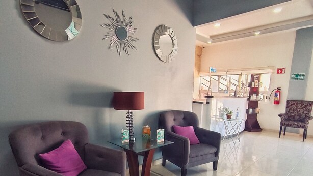 A lobby with two armchairs, a glass-top table, and decorative mirrors on the wall. - Noas hotel (Matamoros)