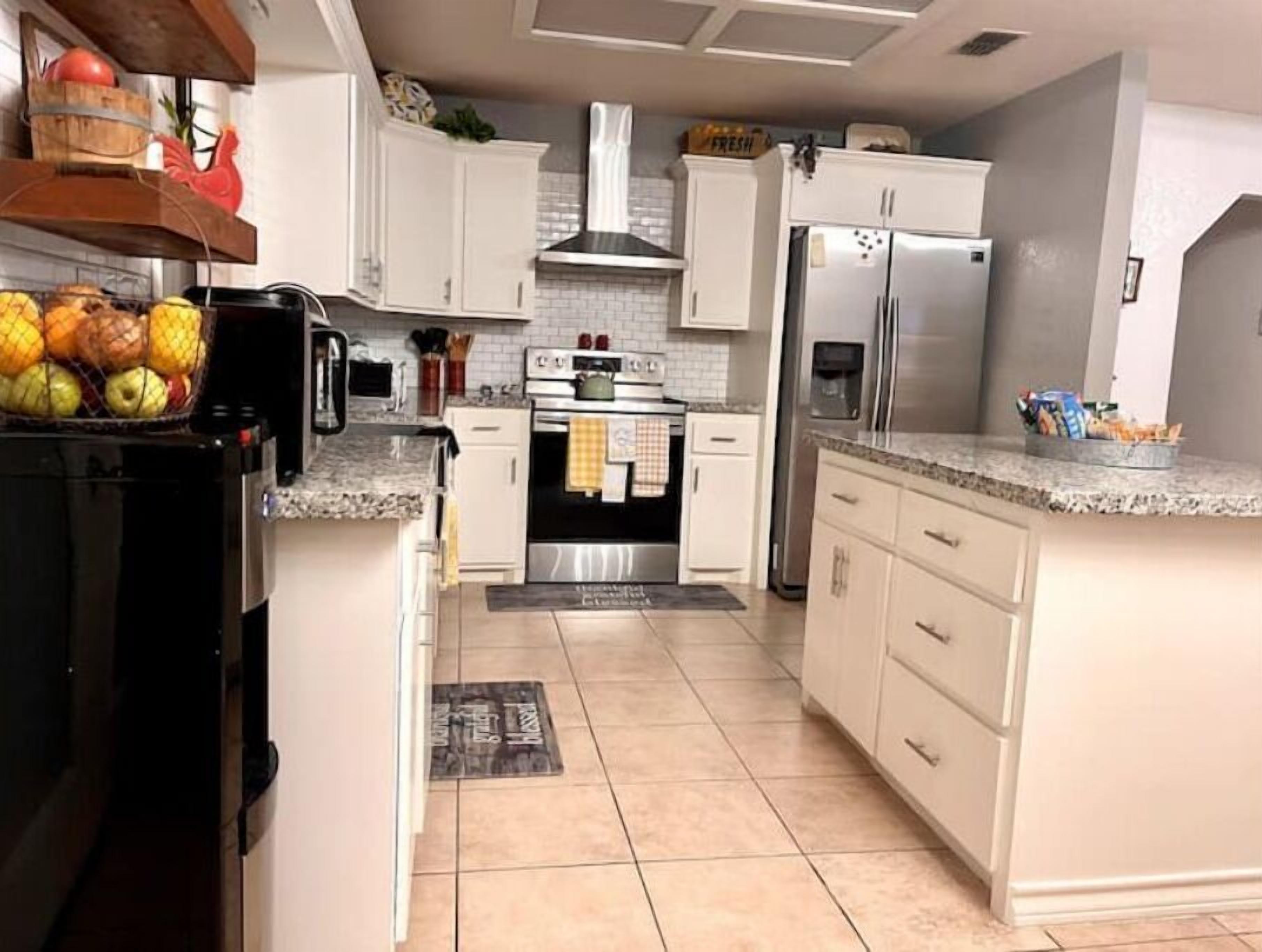 A kitchen with white cabinets, a stainless steel refrigerator, a stove, and a sink.