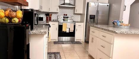 A kitchen with white cabinets, a stainless steel refrigerator, a stove, and a sink.