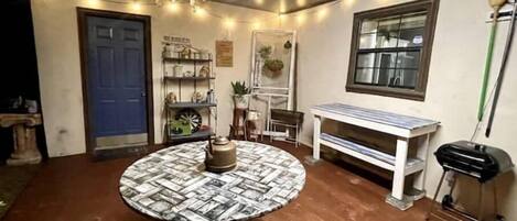 Une pièce comprenant une table ronde recouverte d’une nappe à motifs, un lustre, une bibliothèque, une fenêtre et un banc.