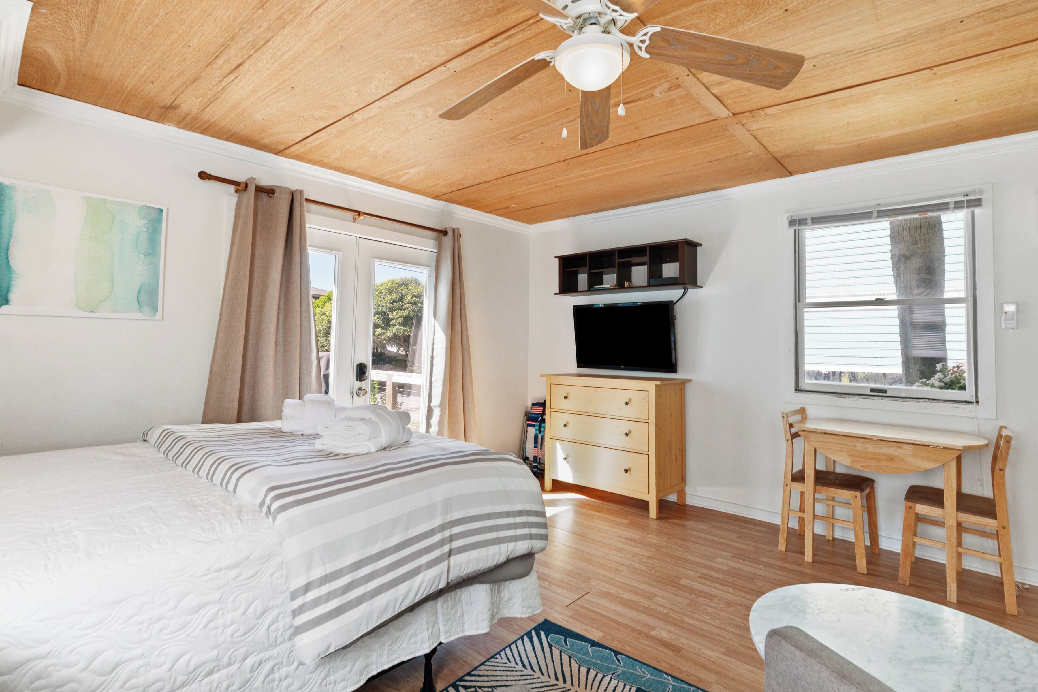 Une chambre à coucher comprenant un lit, un bureau, un téléviseur et un ventilateur de plafond.
