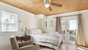 Un dormitorio con una cama, una silla, una mesa redonda, un ventilador de techo y una ventana con persianas.