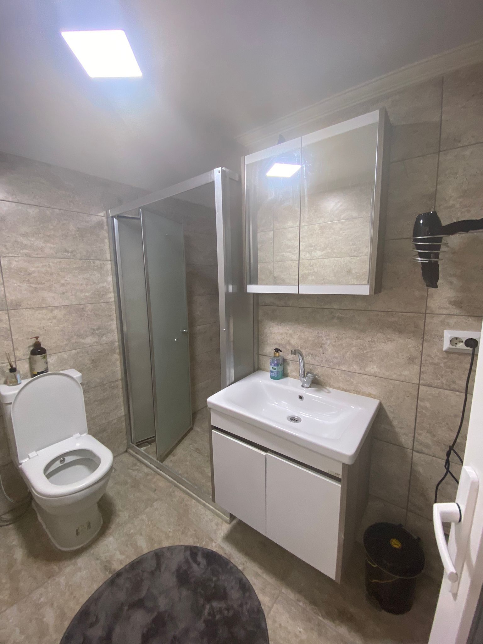 A bathroom with a toilet, sink, mirror, and shower.