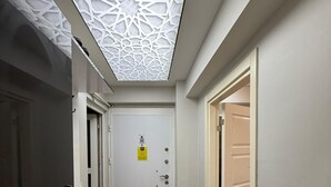 A hallway with a white door, a desk, and a patterned ceiling. - Mertcan Pansiyon (Karabük)