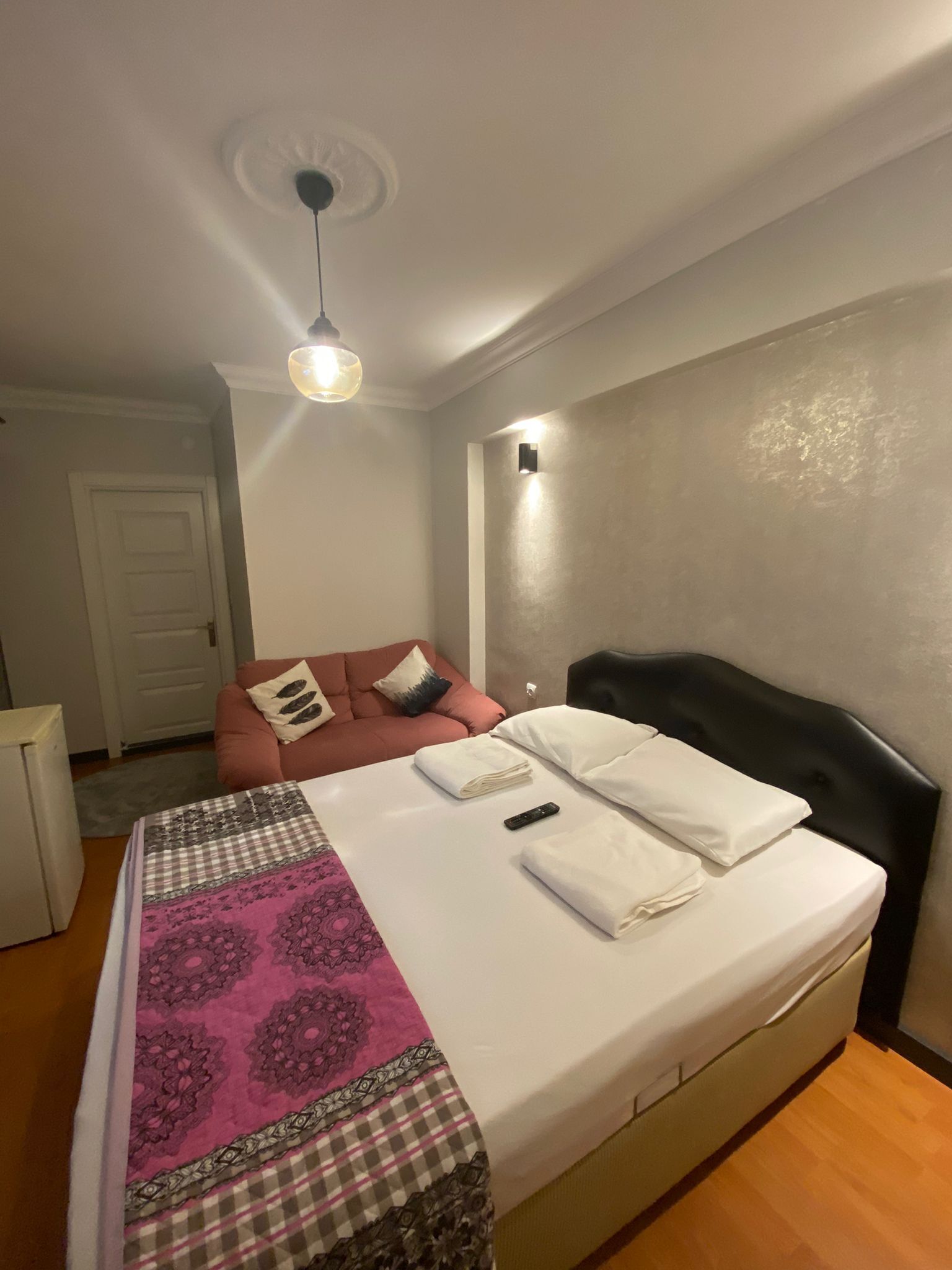 A bedroom with a bed, a nightstand, a red sofa, a ceiling light, and a wall-mounted light.