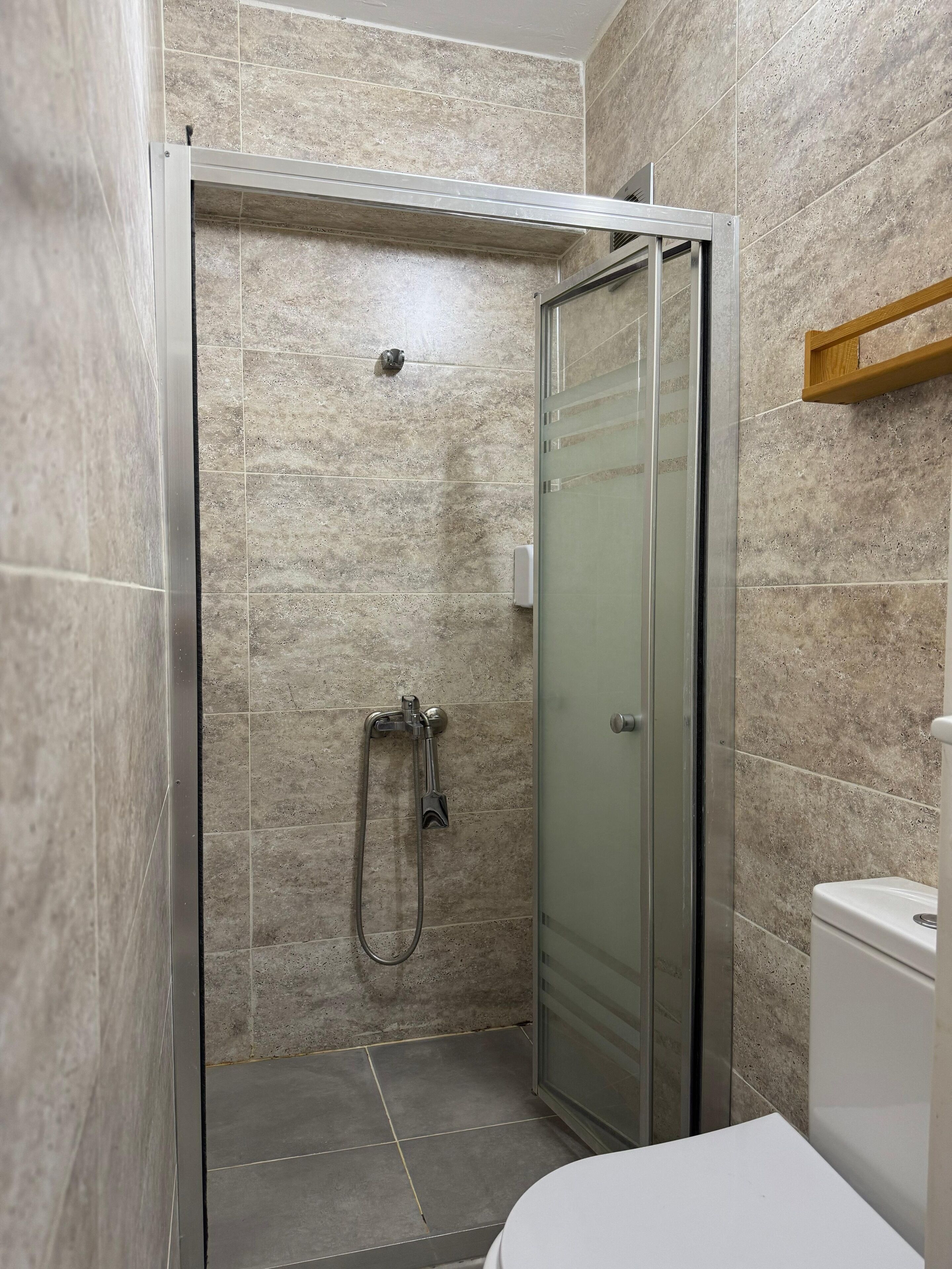Ducha con mampara de vidrio, cabezal de ducha de mano y grifo empotrado.