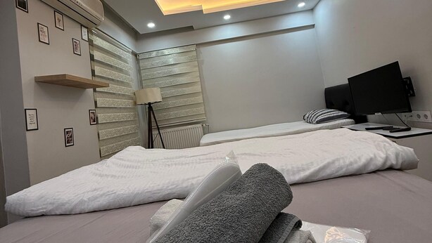 A modern hotel room with a ceiling light, air conditioning unit, and a bed with a white mattress and gray towels. - Mertcan Pansiyon (Karabük)