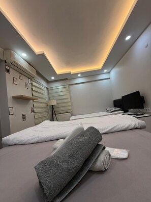 A modern hotel room with a ceiling light, air conditioning unit, and a bed with a white mattress and gray towels. - Mertcan Pansiyon (Karabük)