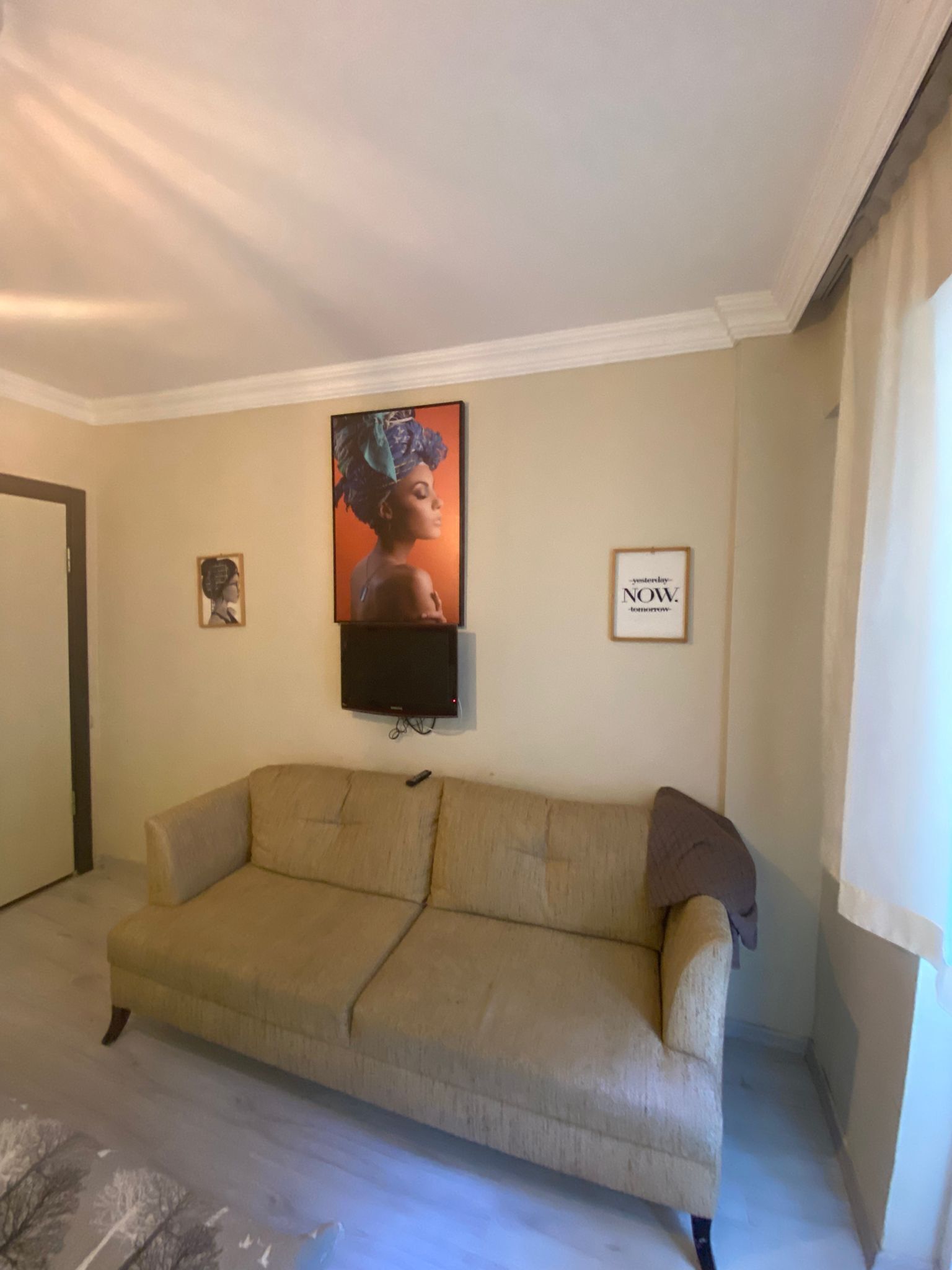Uma sala de estar com um sofá bege, uma TV de tela plana na parede e duas fotos emolduradas.