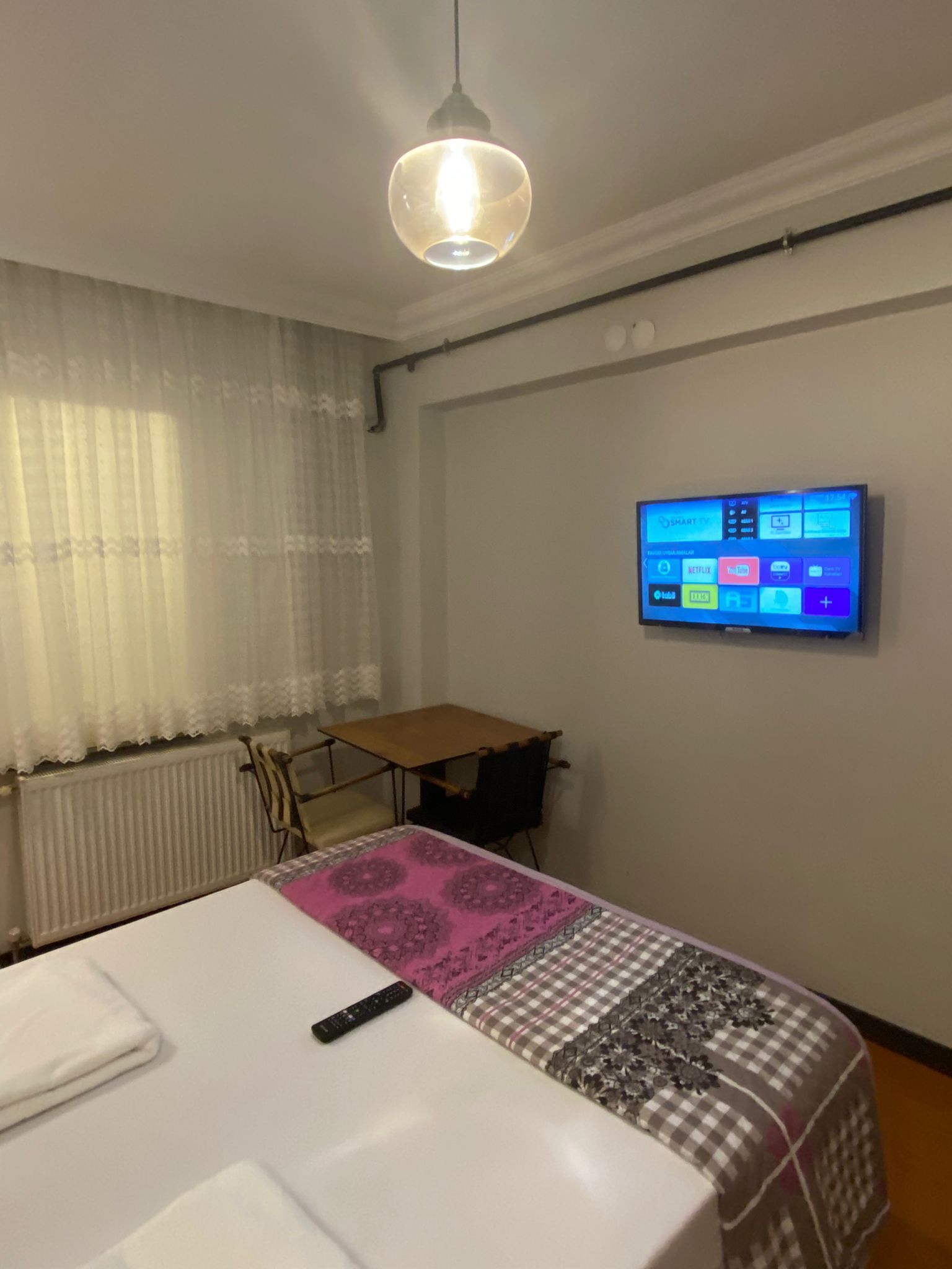 A hotel room with a bed, a desk, a TV mounted on the wall, and a window with curtains.