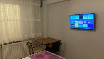 A hotel room with a bed, a desk, a TV mounted on the wall, and a window with curtains.