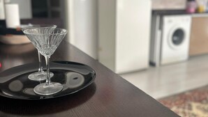 A dining table with a black tray holding two clear glasses. In the background, there is a kitchen area with a washing machine and a refrigerator. - Mertcan Pansiyon (Karabük)