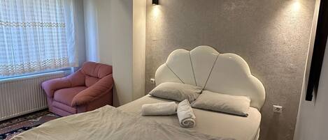 Un dormitorio con una cama grande, una silla rosa y una lámpara colgante.