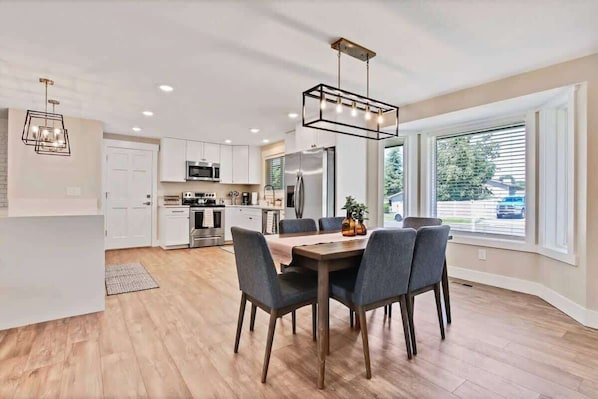 A modern kitchen with white cabinets, a dining table with chairs, and a pendant light.