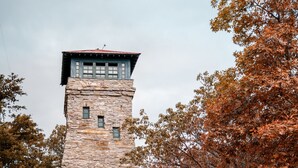 Un edificio de piedra con una torre, un cartel que indica 'Punto más alto de Alabama', y un letrero para 'Parque Estatal Cheaha Elevación'.