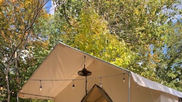 Alojamiento en carpa con terraza de madera, una mesa con un farolillo y vistas a los árboles circundantes.