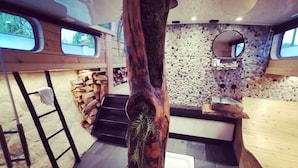 Un interior rústico con un gran tronco de árbol como pieza central, una pared de piedra y una escalera de madera.