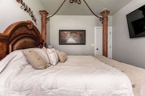 A bedroom with a four-poster bed, a framed picture on the wall, and a television mounted on the wall.