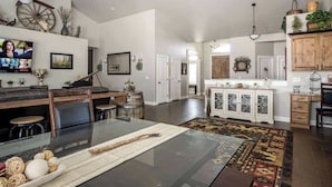 Ein großzügiger Wohnbereich mit einem Esstisch mit Glasplatte, einem großen Teppich und einer Küche mit weißen Schränken.