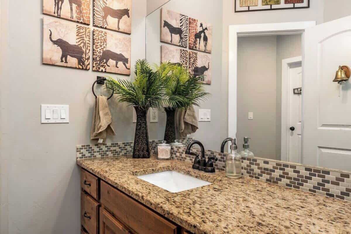 Een badkamer met een granieten aanrecht, een wastafel, een spiegel en wanddecoratie met dieren.