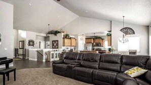 Ein geräumiges Wohnzimmer mit Ledersofa, einem Klavier und Blick auf die Küche und den Essbereich.