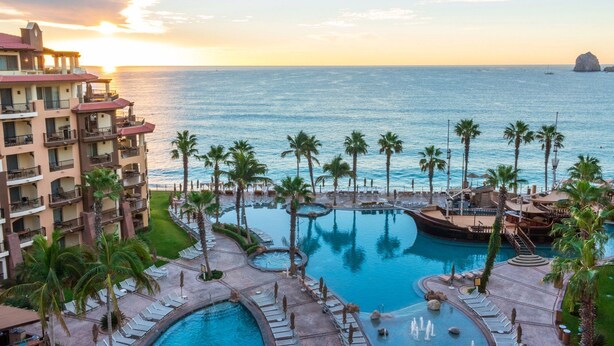 Ein Resort mit großem Pool, Palmen und Blick auf den Ozean bei Sonnenuntergang.