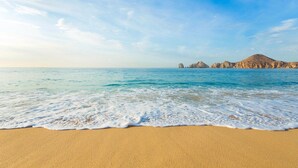 Ein Strand mit klarem, blauem Wasser, sanften Wellen und Felsen in der Ferne.